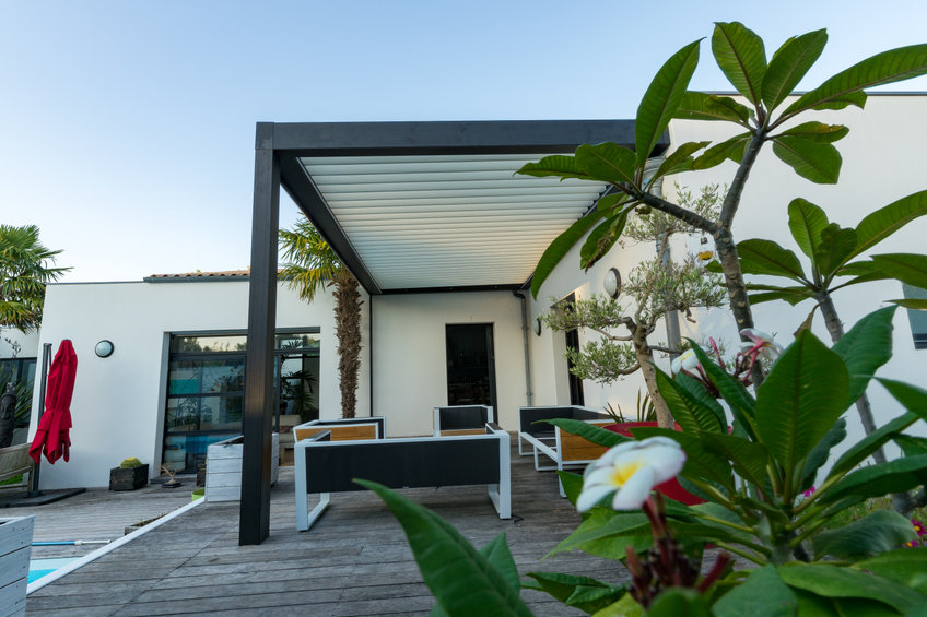 trendy outdoor patio pergola. garden lounge, chairs, metal grill surrounded by landscaping